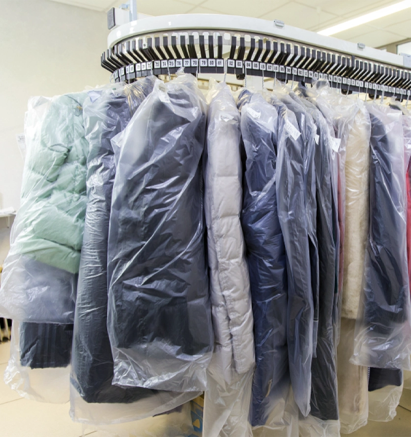A row of coats and jackets covered in plastic hangs on a numbered conveyor rack in a dry cleaning facility.