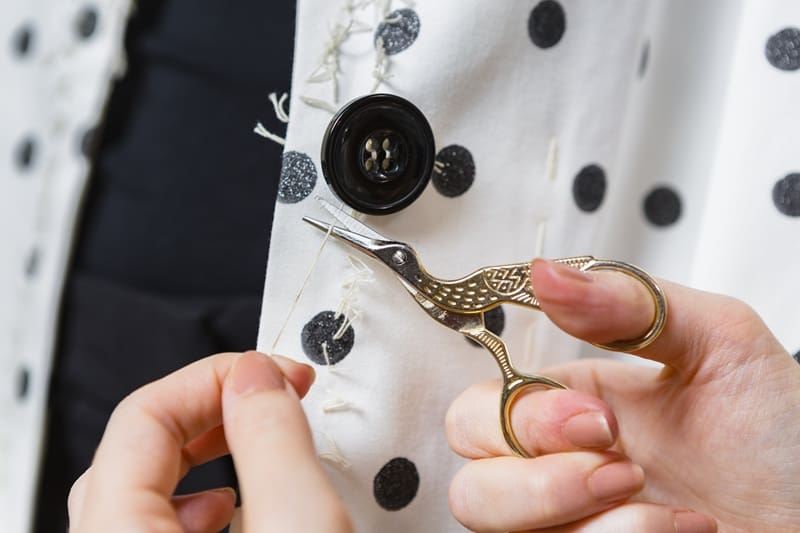 Close-up of hands using small scissors to cut white thread from a polka dot fabric with a large black button attached.
